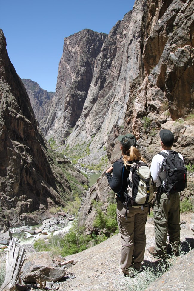 Two people with backpacks on a route looking out at an inner canyon and river below