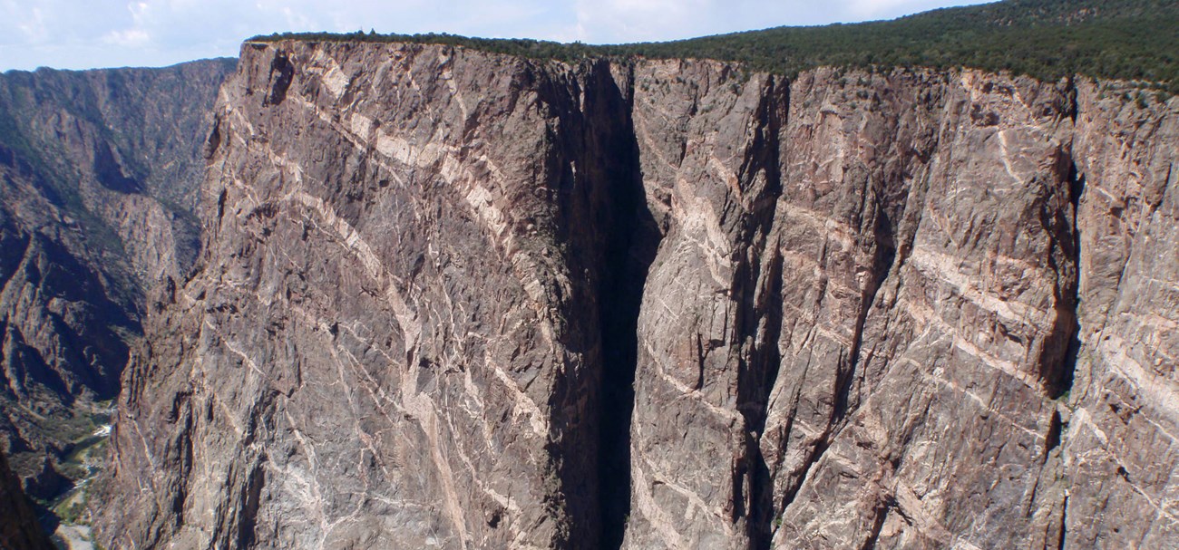 Tall vertical canyon wall with sections of greyish black and lighter brown and pink rock