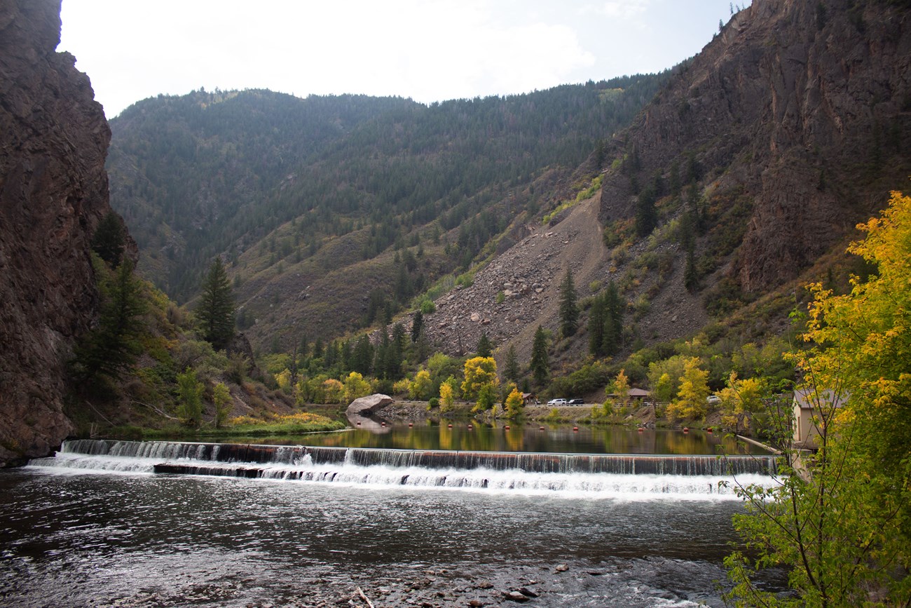 A small dam and river with fall foliage and canyon walls on the sides