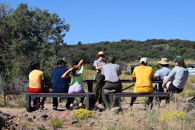 A park ranger stands in front of a group seated at picnic tables