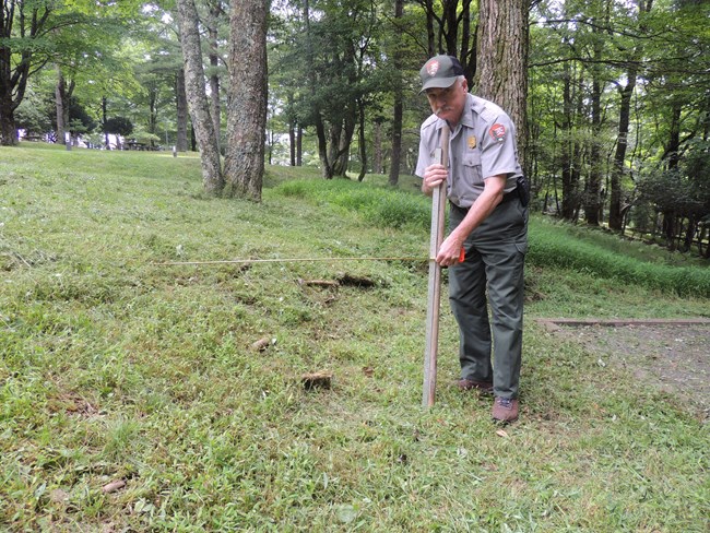 NPS Employee measuring embankment at campground.