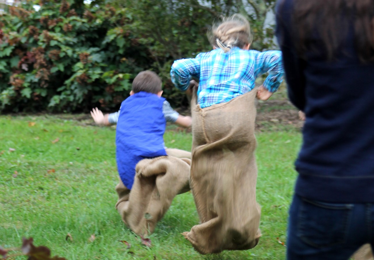 Children jumping through the grass during a sack race.