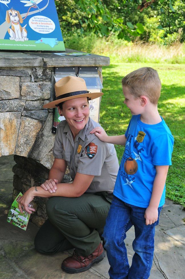 A young boy speaks with a kneeling female park ranger. They are standing in front of a small stone archway.