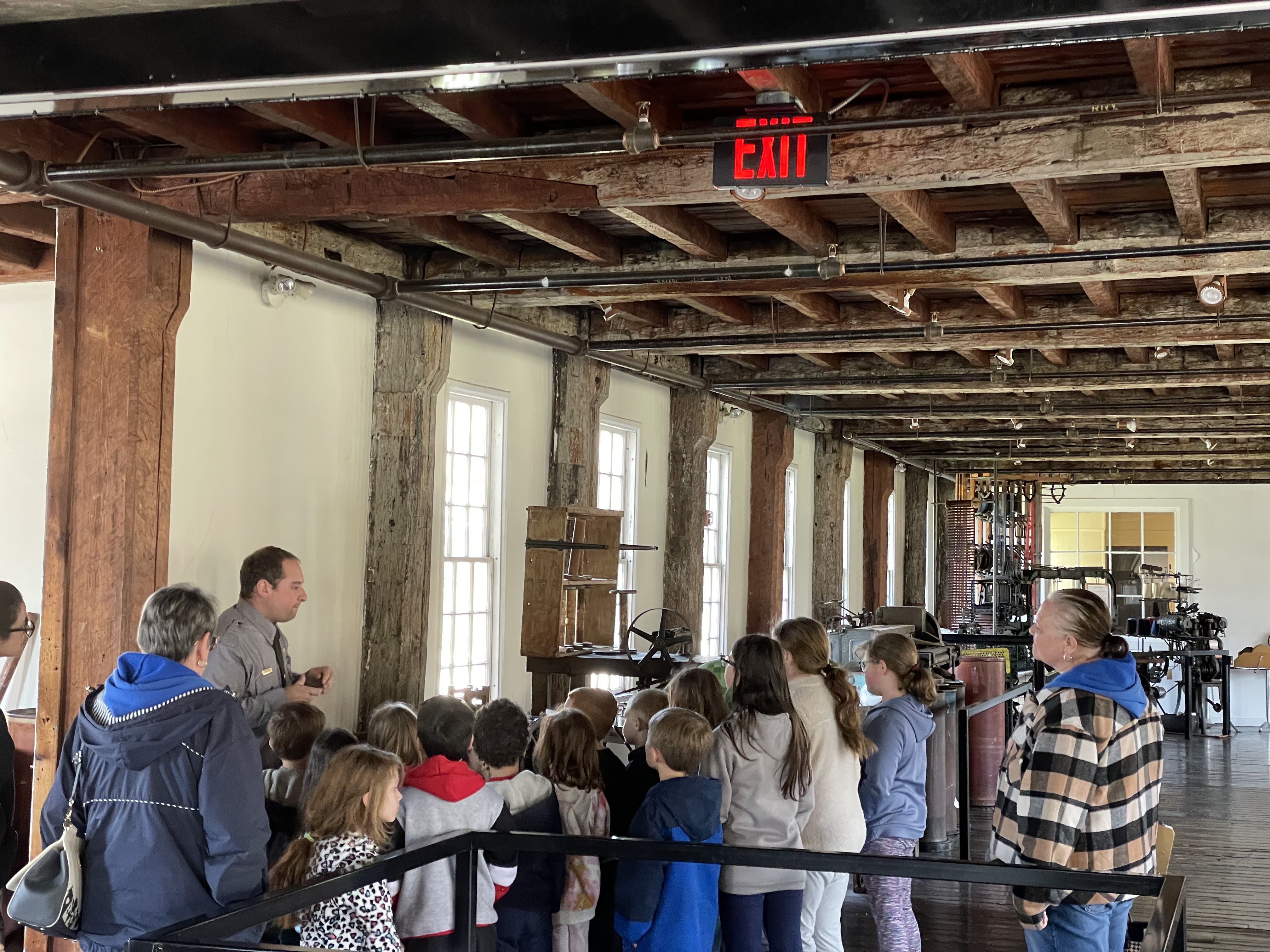 a group of children listening to a ranger in uniform by machines