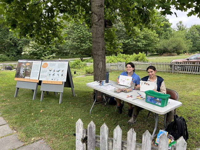 Two female interns in polos with science activities underneath a tent