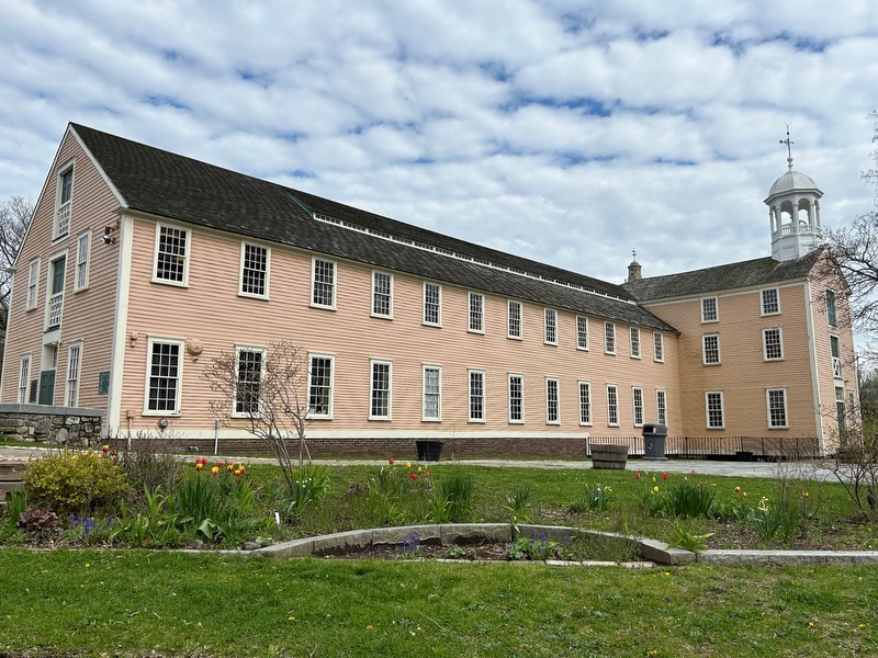 Two story yellow mill building with flowers in the foreground