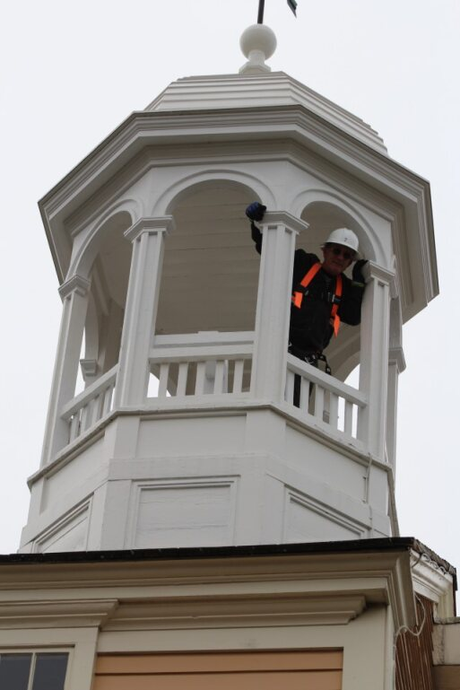 Man with safety equipment waves from Bell Tower cupola