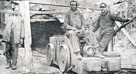 historic photo of coal miners in a mine car outside mine entrance