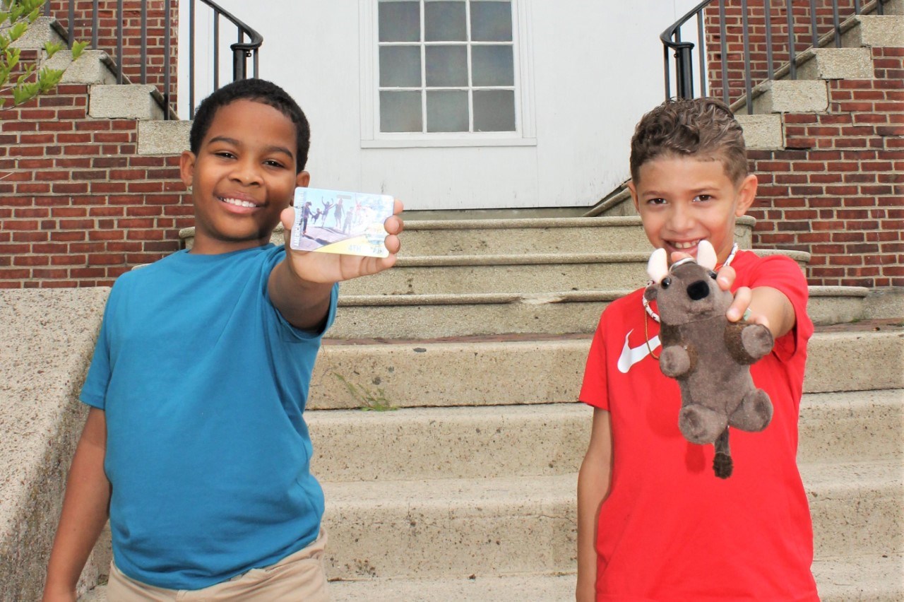 Two kids with one holding a pass and another holding a stuffed animal buffalo.