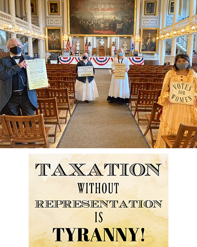 three women and one man in period clothing holding signs in Faneuil Hall. Below is a poster that says "Taxation without Representation is Tyranny"