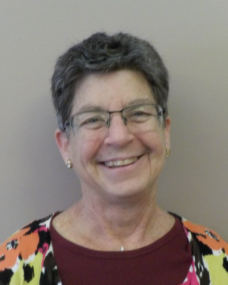 KarenHiller Head shot of a middle aged woman with short black and white hair, modern glasses gold earrings and colorful floral shirt.