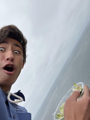 Intern Keanu making a silly face with wide eyes eating a salad with the ocean in the background