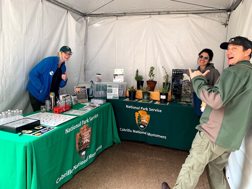 The science education and outreach team poses at their booth during the Science and Engineering Festival, complete with live plants, activities, and promotional materials.