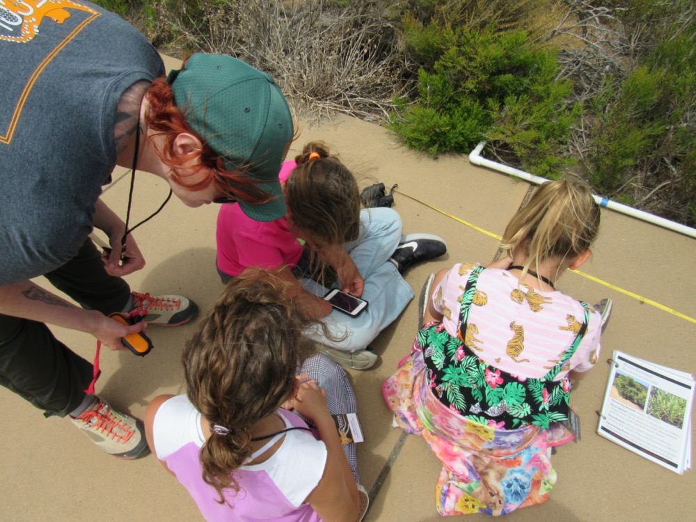 AAAS IF/THEN® Ambassador Samantha Wynns stoops next to campers from EcoLogik, Cabrillo’s free STEM summer camp for girls, as they take data. Samantha and the students all hold instrumentation.