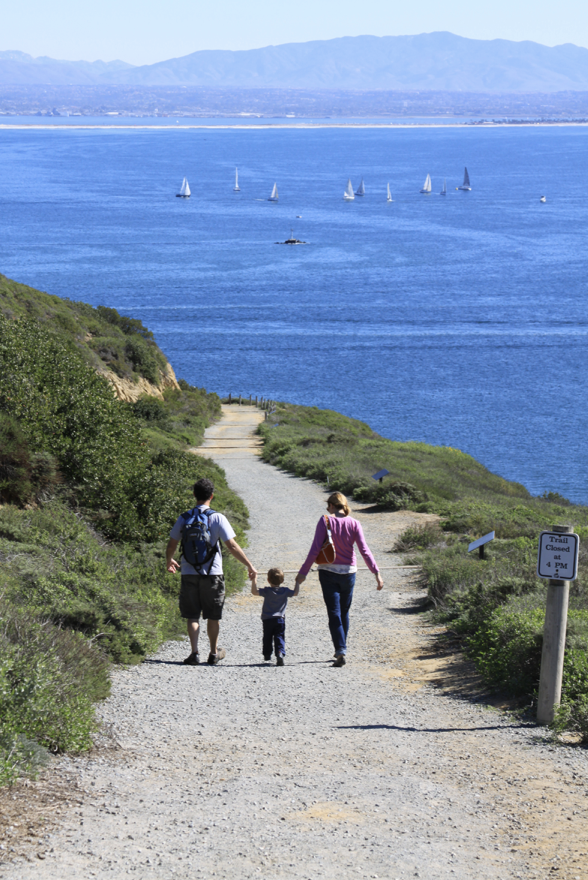 A family walks down a slopping trail towards the ocean.