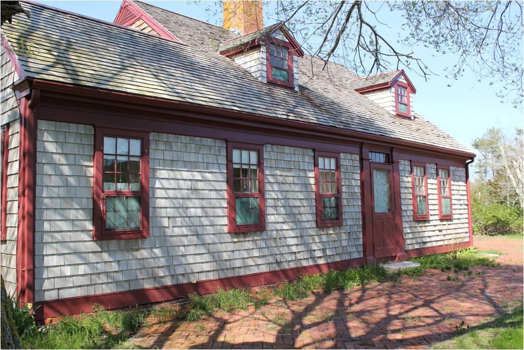 A historic shingled house with red shutters and windows.