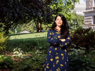 U.S. Poet Laureate Ada Limon poses for the camera in a dark blue dress in front of a garden.