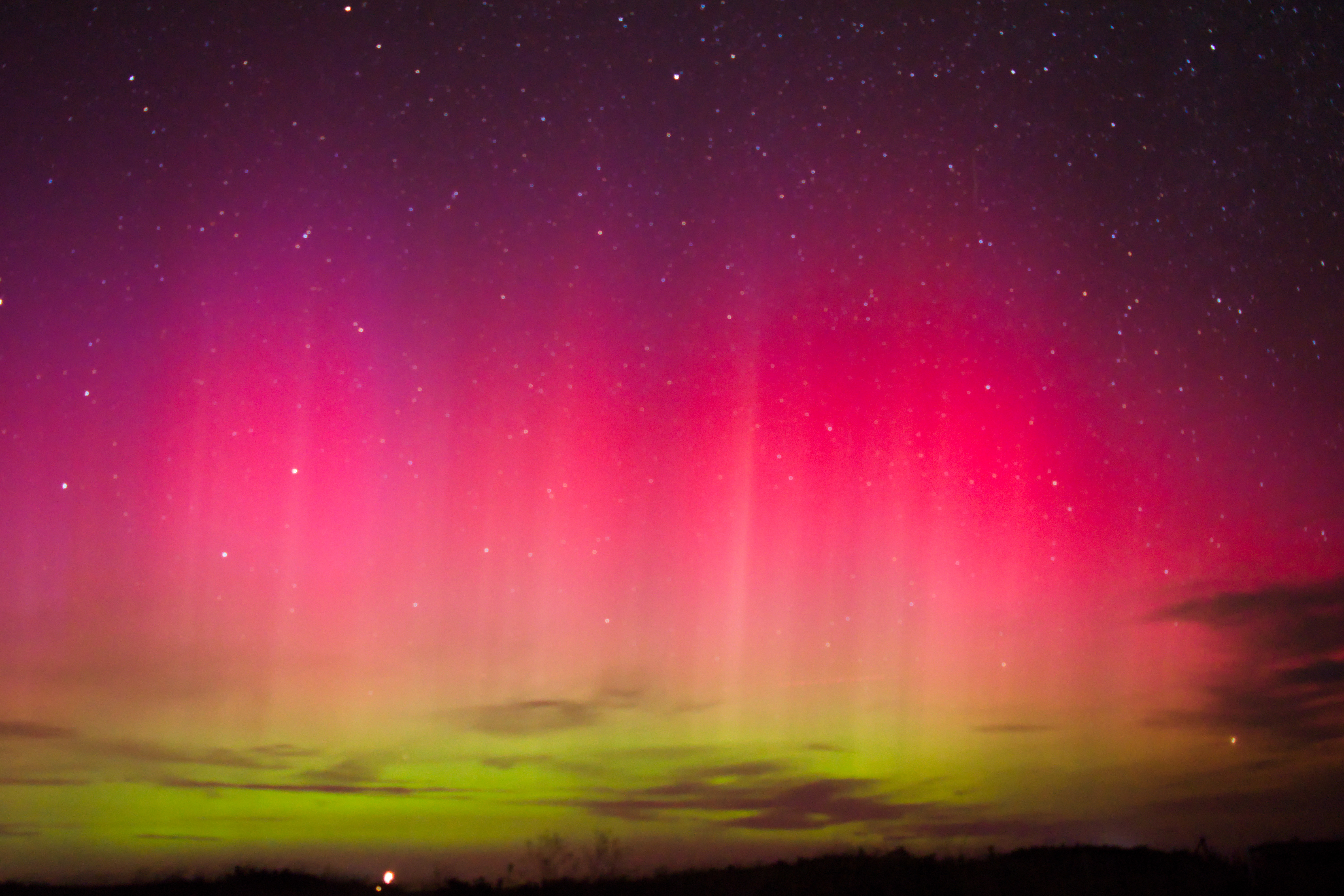 Shades of purple, pink and green shimmering lights over a stary night landscape.