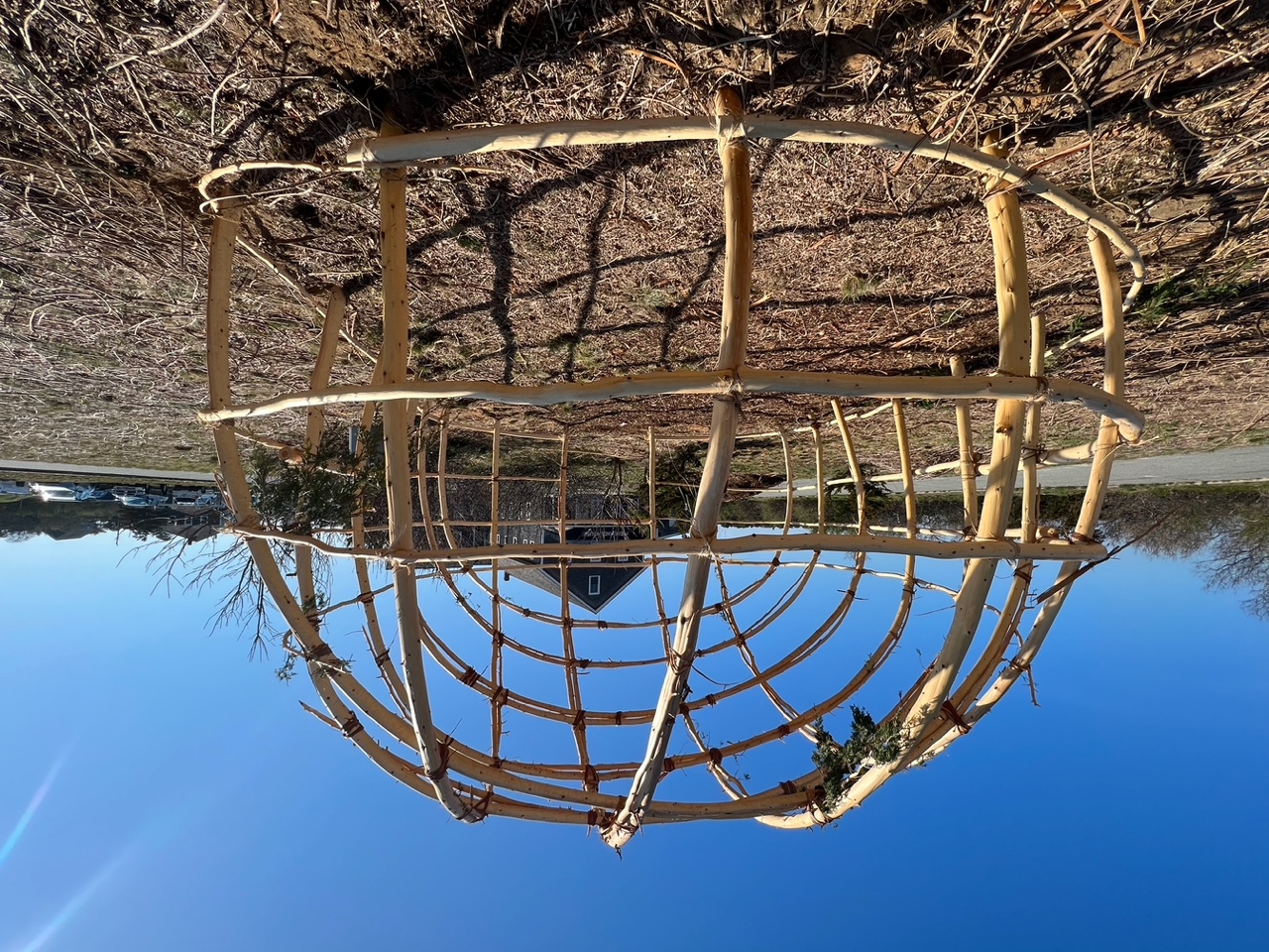 A wetu structure stands against a bright blue sky.