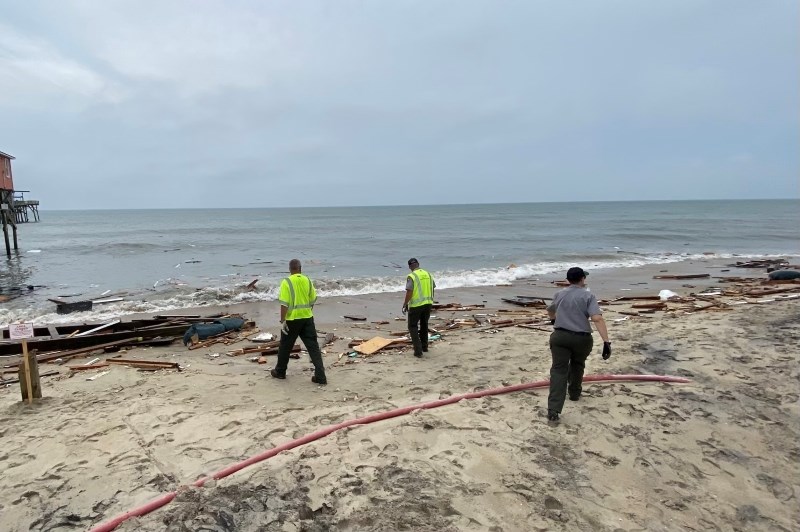 Three National Park Service employees collect house debris from the beach.