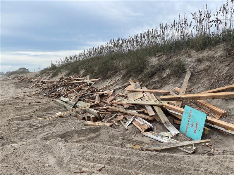 Piles of house collapse debris lined up along a dune near beach.