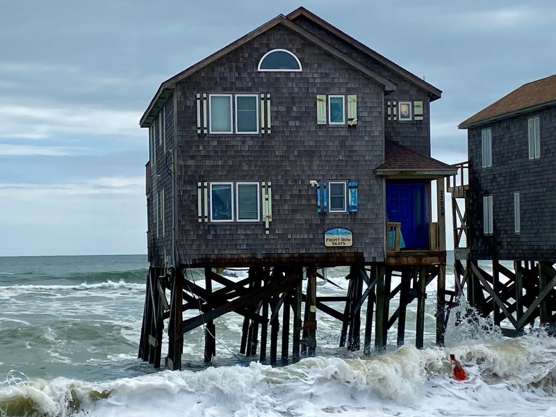 Photo of leaning house on pilings in the ocean.