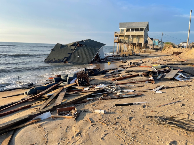 Photo of a collapsed house and debris on the beach.
