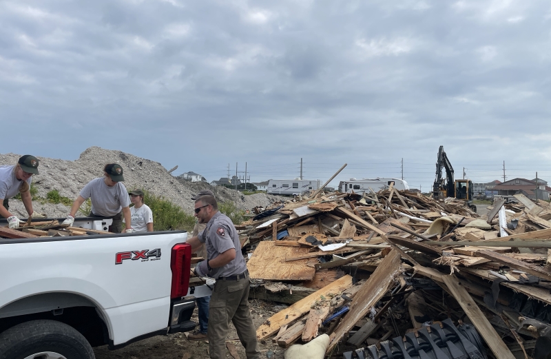 Four people in uniform offload a truck full of wooden debris.