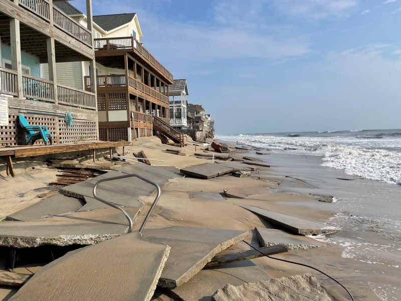 Photo of broken concrete in front of houses at the beach.