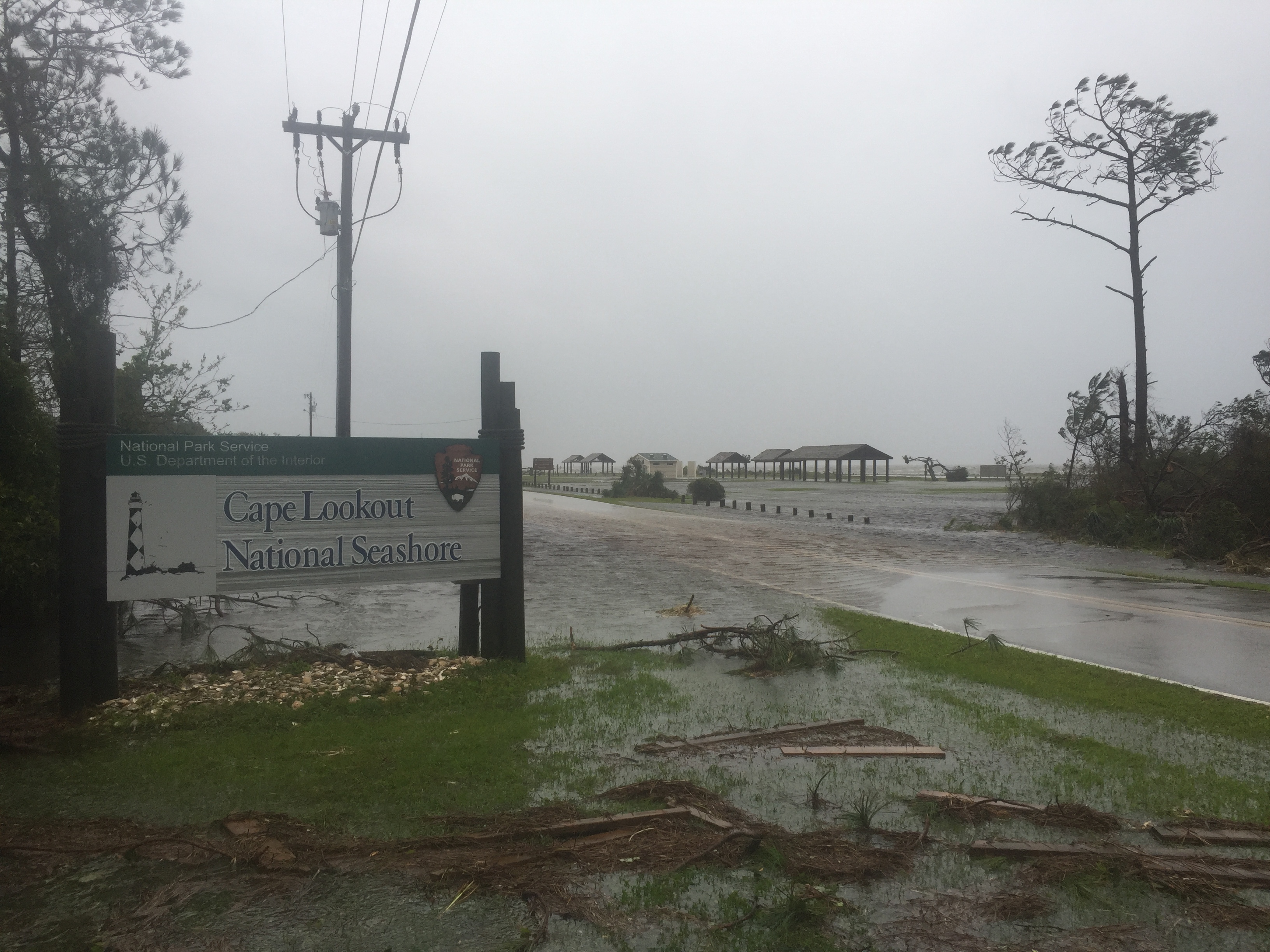 Flood waters and downed limbs surround the entrance sign for Cape Lookout National Seashore.