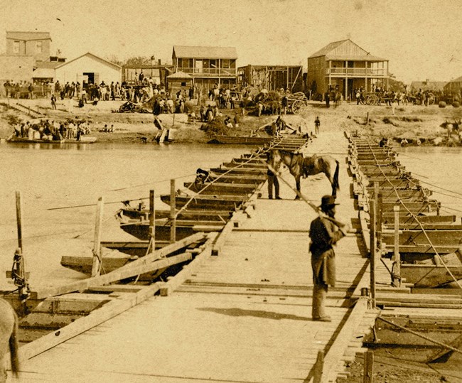 Black soldier standing on a pontoon bridge with buildings in the background