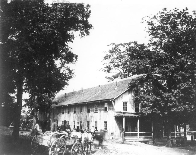 Large two-story building with horse-drawn wagon carrying several men in front.