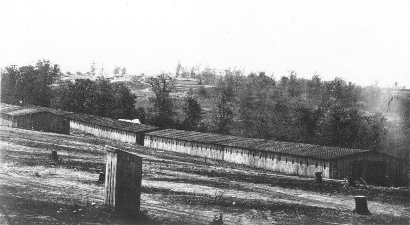 Long one-story building in the foreground with trees and additional buildings in the background during the Civil War.