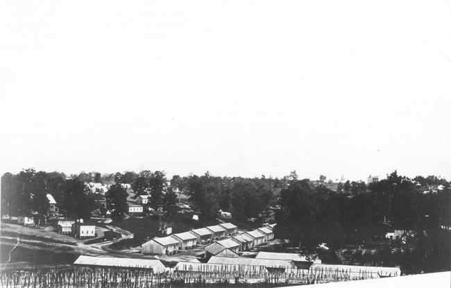 Long line of wagons and wooden buildings interspersed by trees during the Civil War