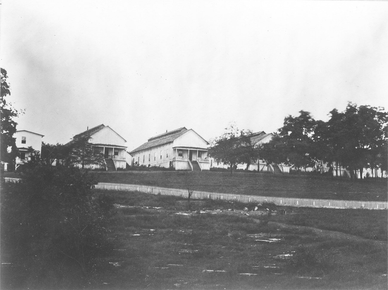 Rectangular wooden buildings with a field and trees in front during the Civil War.