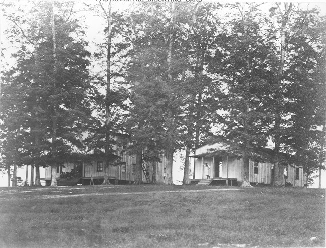 Two wooden buildings surrounded by many trees during the Civil War.