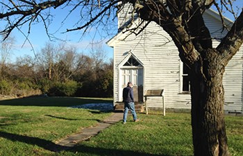 Man walks toward sign in front of old wooden church building.