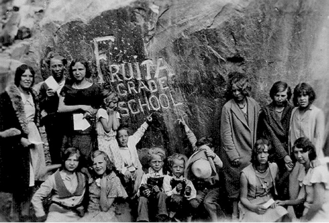 Black and white photo of school children and adults beside a rock carved with "Fruita Grade School"