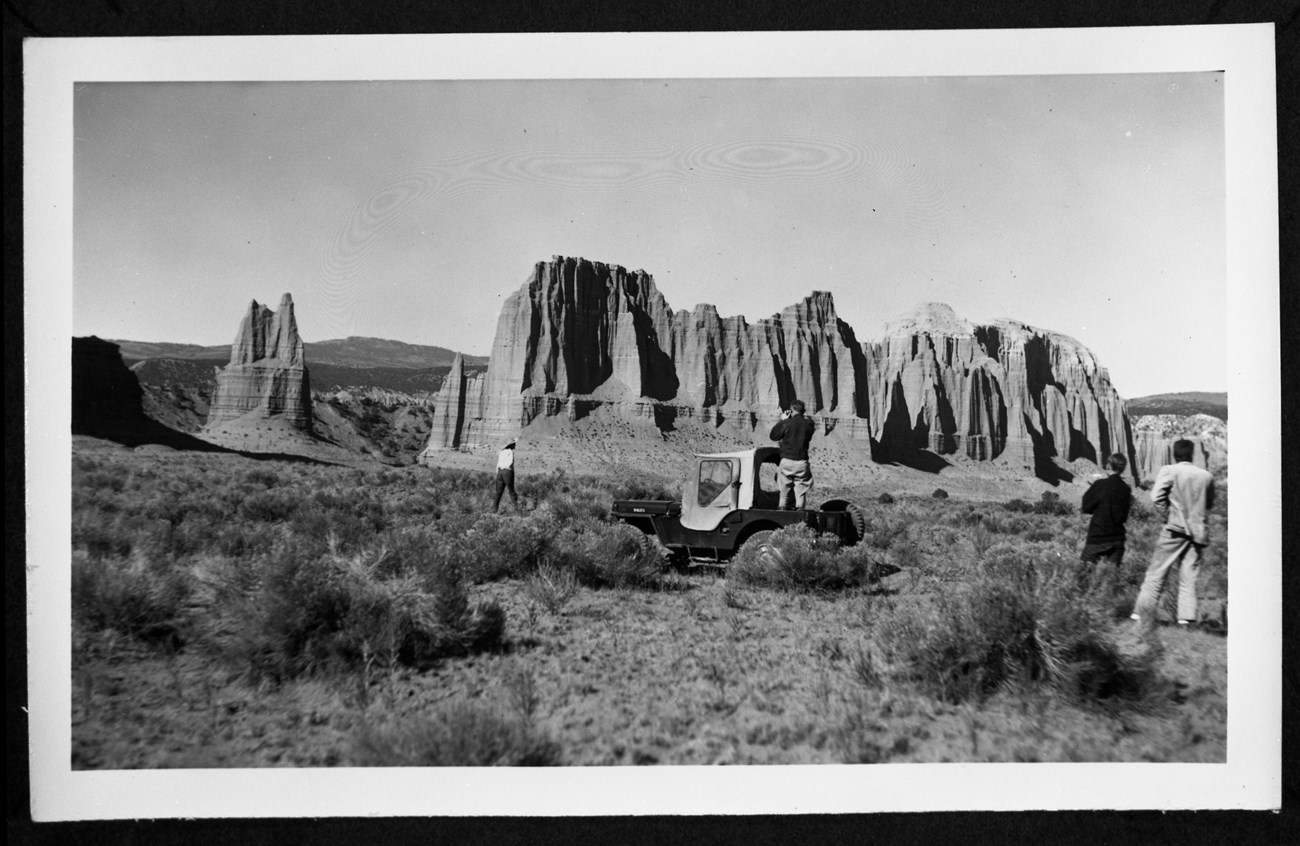 Black and white photo of visitors taking photos of large monoliths.