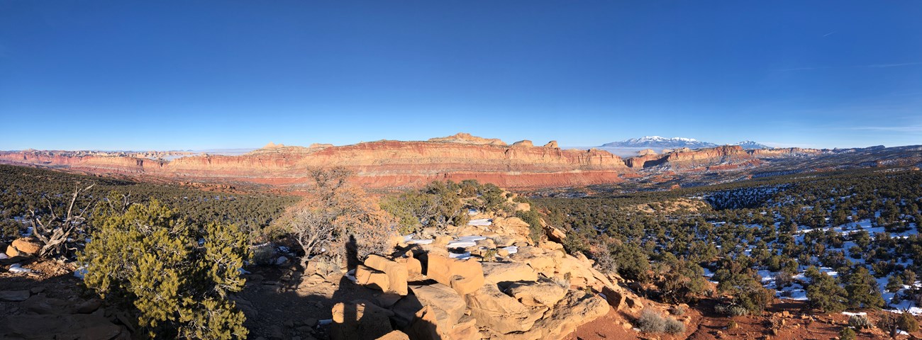 Blue skies are over steep cliffs and a snow-covered mountain many miles away.