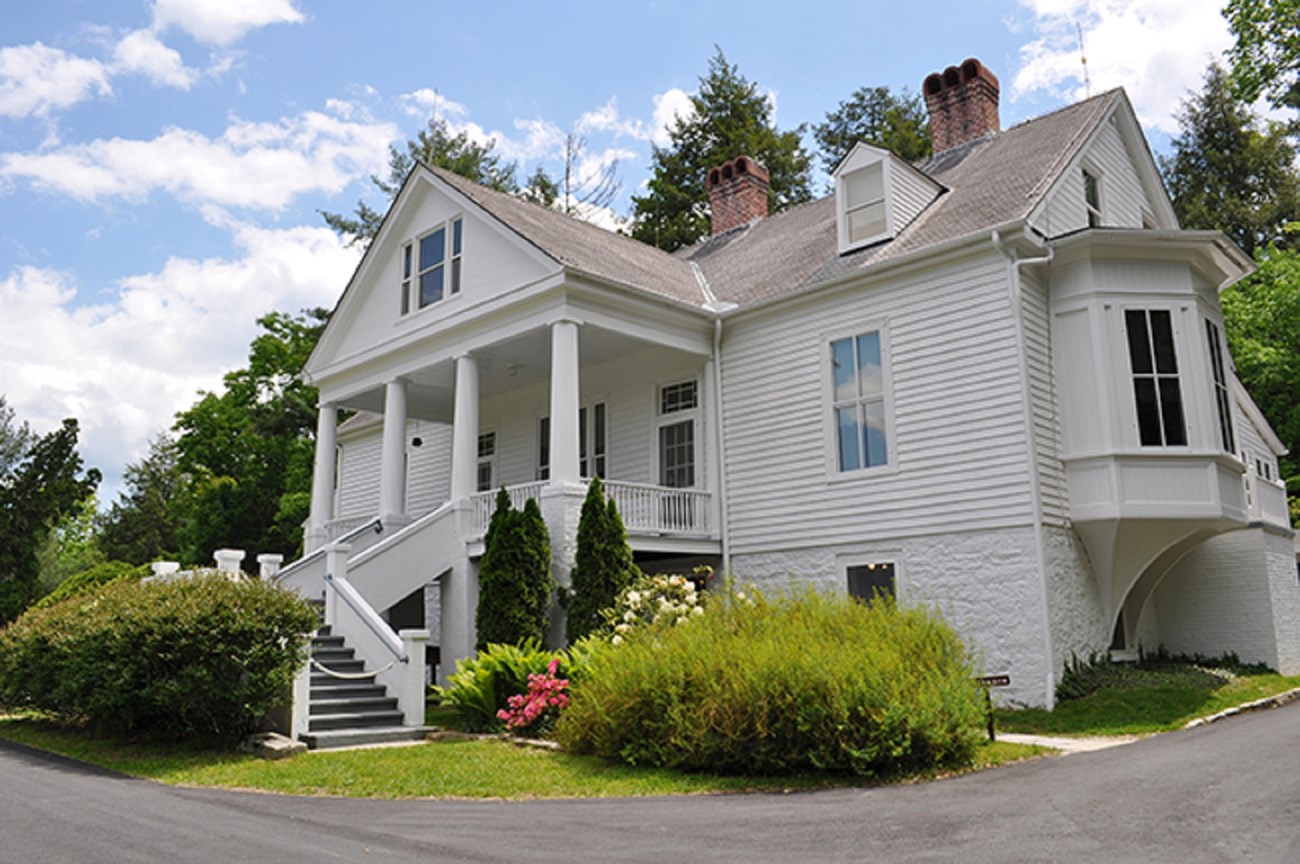 Image of Sandburg Home, a large three story white painted house with stairs leading to a second story porch in front and a bay window on the right side.