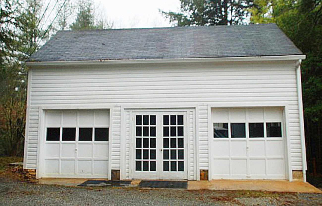 Image of front of house garage, a single story white painted building with 2 garage doors and a french door in the middle