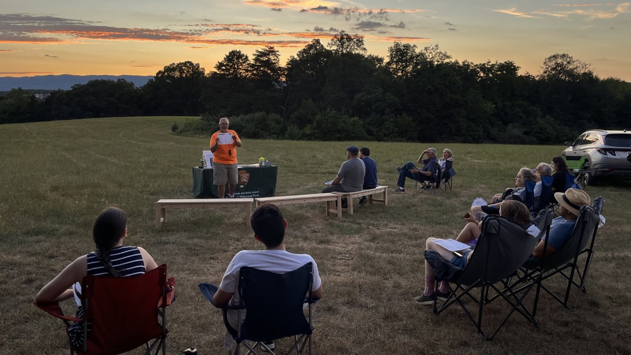 Shenandoah Astronomical Society Volunteer National Park Service volunteer talks to a seated crowd underneath a sunset sky.