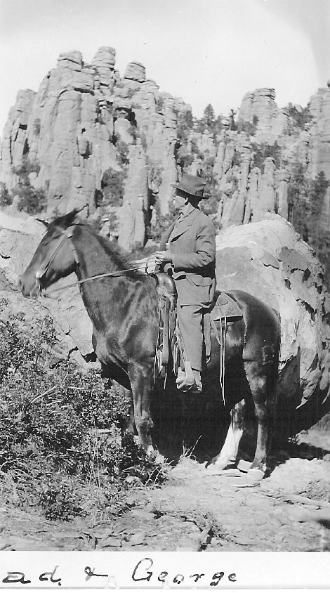 Black and white photo of man on horse in front of rock pinnacles.