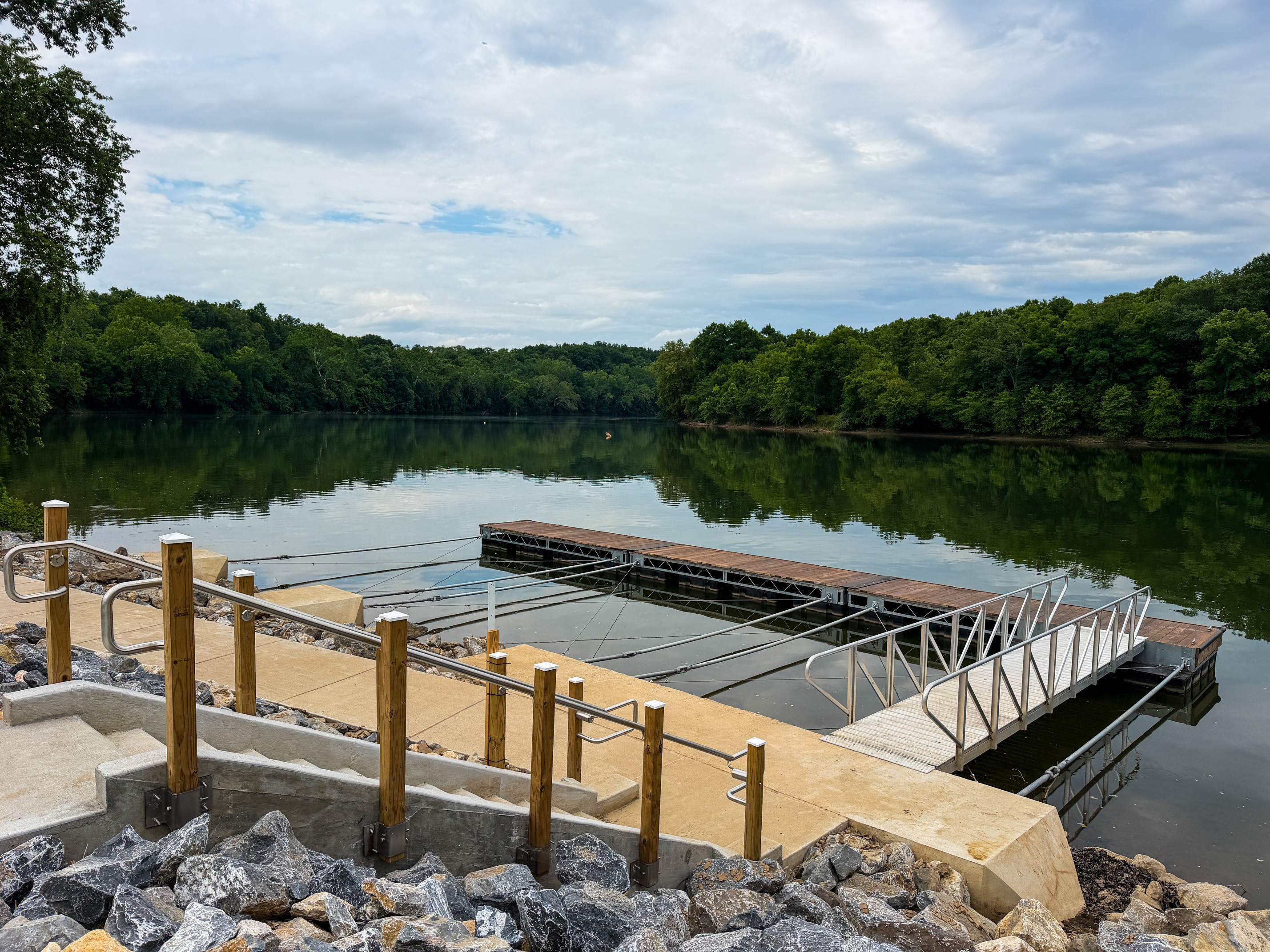 A set of concrete stairs leads down to a metal walkway extending out to a floating boat dock on a river