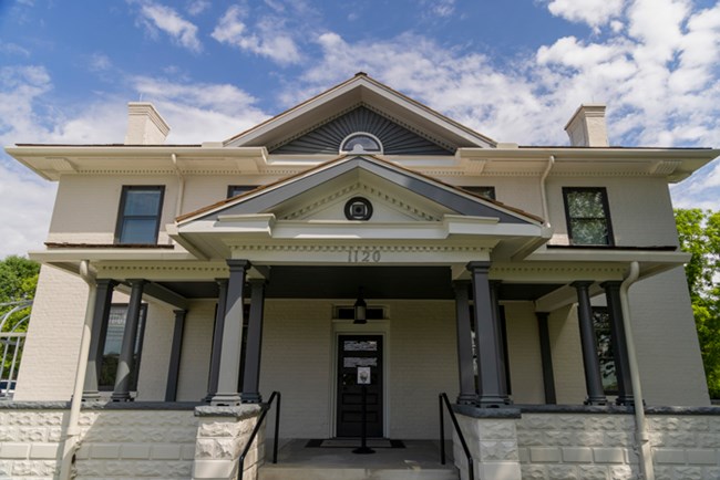 A large two-story house with two rows of five windows on each level and a large, full porch on the first level.