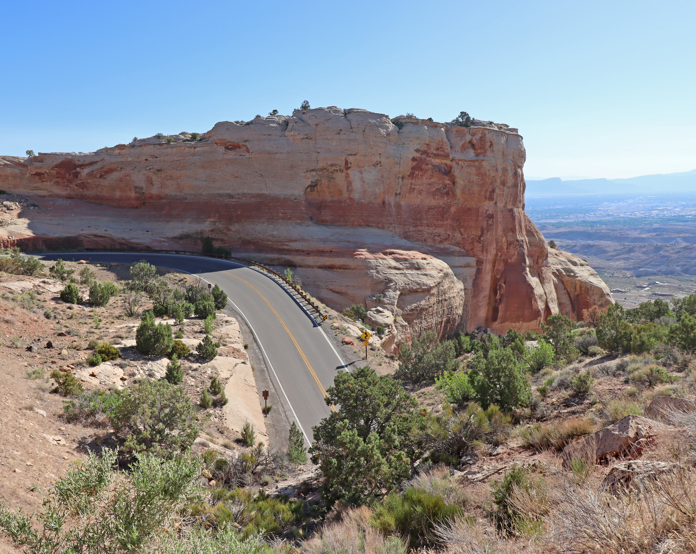 Rim Rock Drive winds its way up canyon walls as it steeply climbs through orange sandstone cliffs and juniper trees in Colorado National Monument.