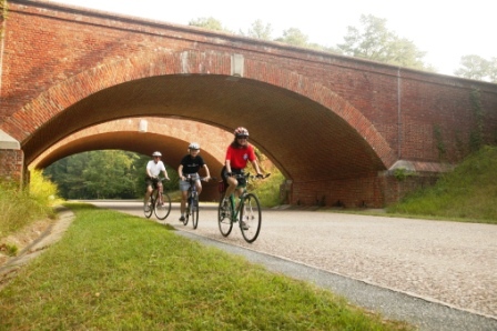 Bicyclists cycle beneath a brick bridge