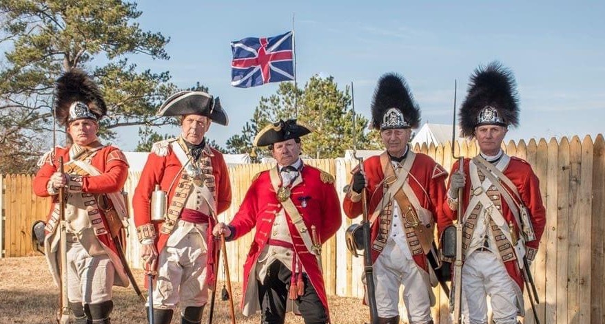 British soldiers.   5 British soldiers in 18th century uniforms (red coats) stand before a British FLag