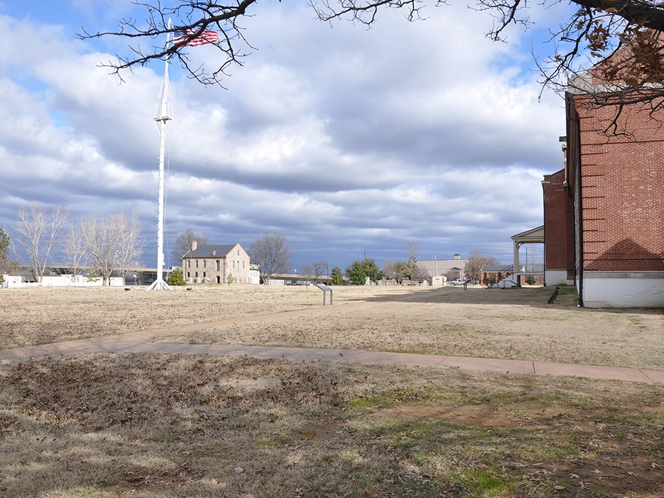 Tents and soldiers camp on the parade ground between fort buildings.